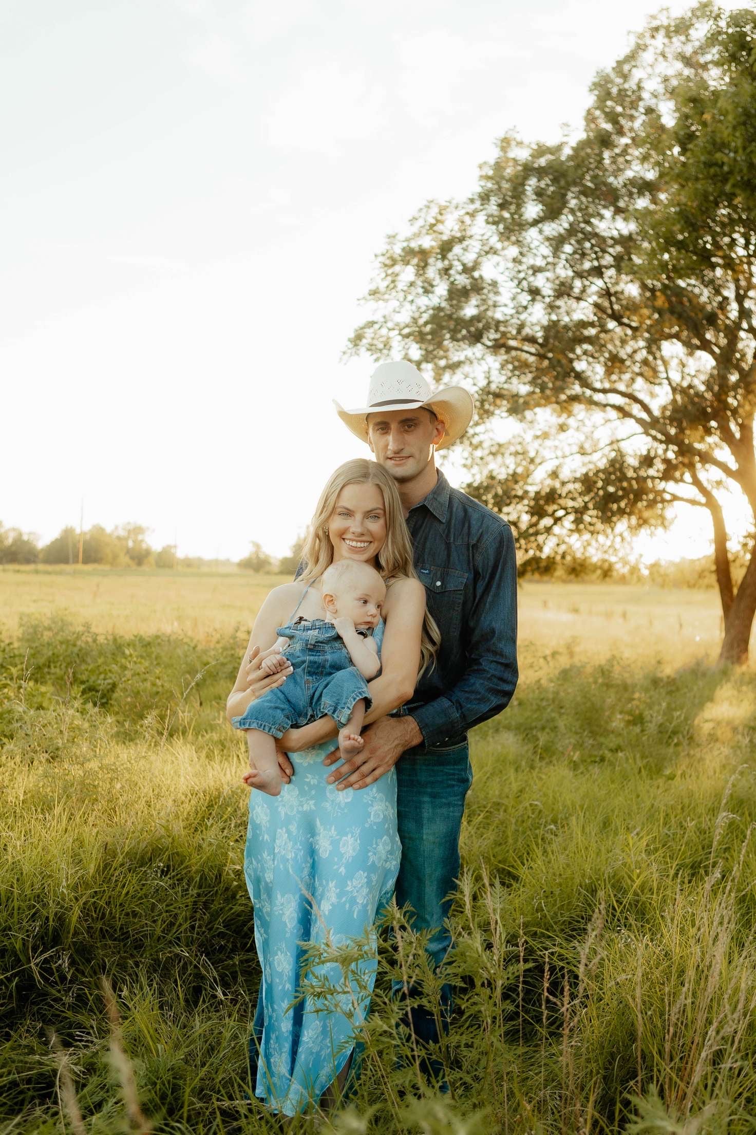 Man and woman standing in a field with a sunset, man wearing a cowboy hat.